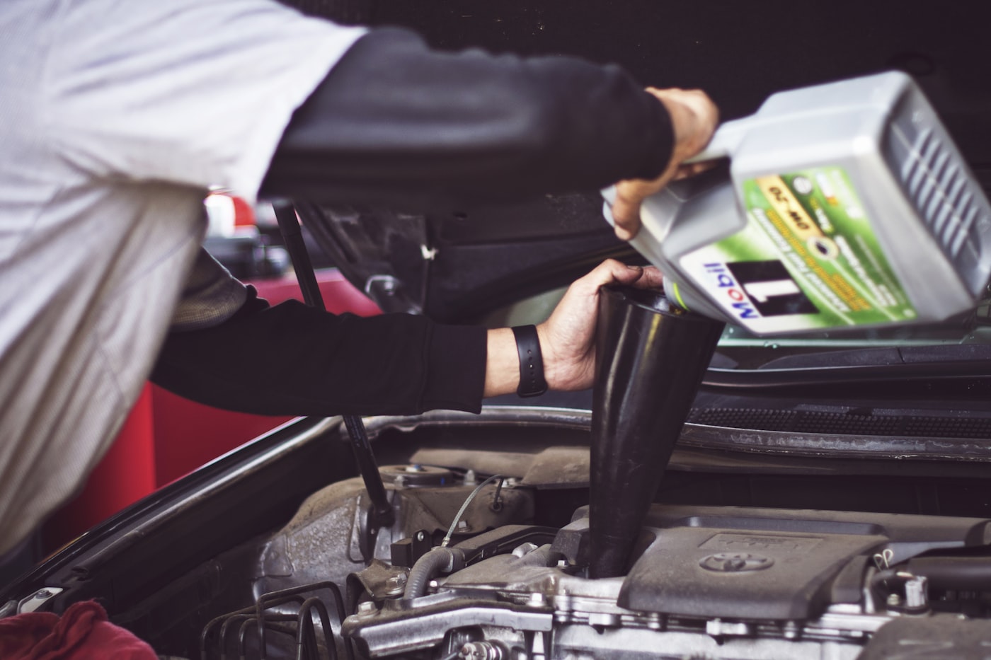 Mechanic topping up oil while working in an engine bay